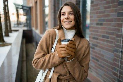 Beautiful cheerful woman holds a cup of hot coffee in her hands in the cold season on the street